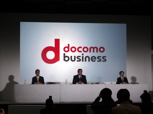 NTTドコモによるNTTコミュニケーションズとNTTコムウェアの子会社化を発表する、NTTドコモの井伊基之社長（中央）ら3社社長。背面のスライドは統合後の2022年1月から使い始める法人事業の新ブランド「ドコモビジネス」