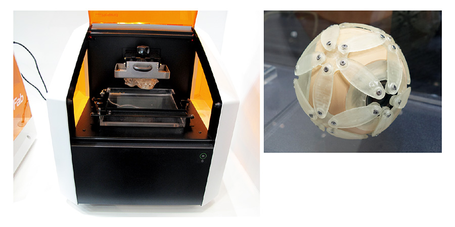 図8●ローランド ディー.ジー.が参考出展した3Dプリンター 下面からプロジェクターで光を当てる方式を採用した。右側の球体スピーカーの表面を覆う部品は、この3Dプリンターで造形したもの。
