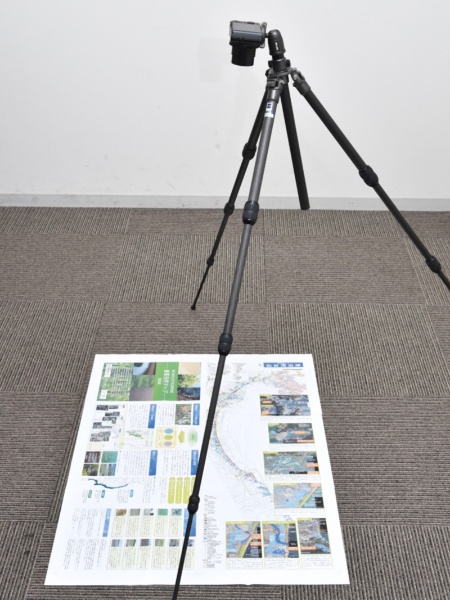 ポスターを床に置いて真上から撮ると、照明の状況によってはカメラの影が落ちることがある。ポスターが大きい場合、高さを稼ぐために大型の三脚が必要となるのも悩ましい